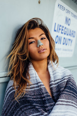 Woman with blanket wrapped around her wearing green Noz sunscreen on her nose