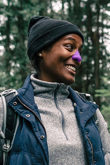 Woman smiling in forest with purple Noz sunscreen on nose