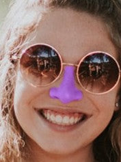 Woman with sunglasses smiling with purple Noz sunscreen on nose