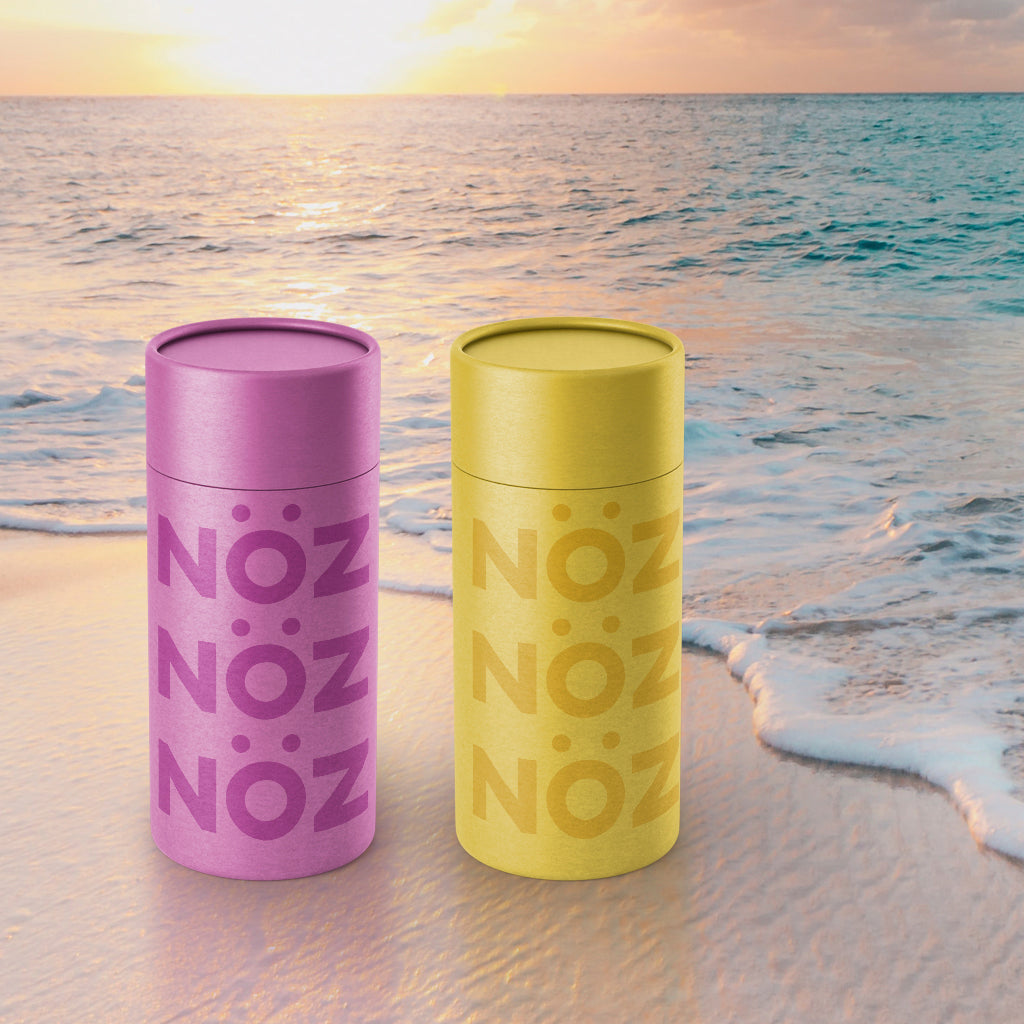 Purple and yellow Noz sunscreen on beach with sunset